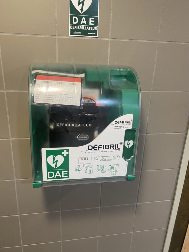 Défibrillateur automatisé externe DAE en boîtier mural vert fixé sur un mur carrelé dans un lieu public, signalétique DAE visible au-dessus de l'appareil