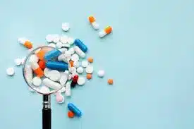 circuit du médicament : comprimés et gélules observés à la loupe sur fond bleu clair